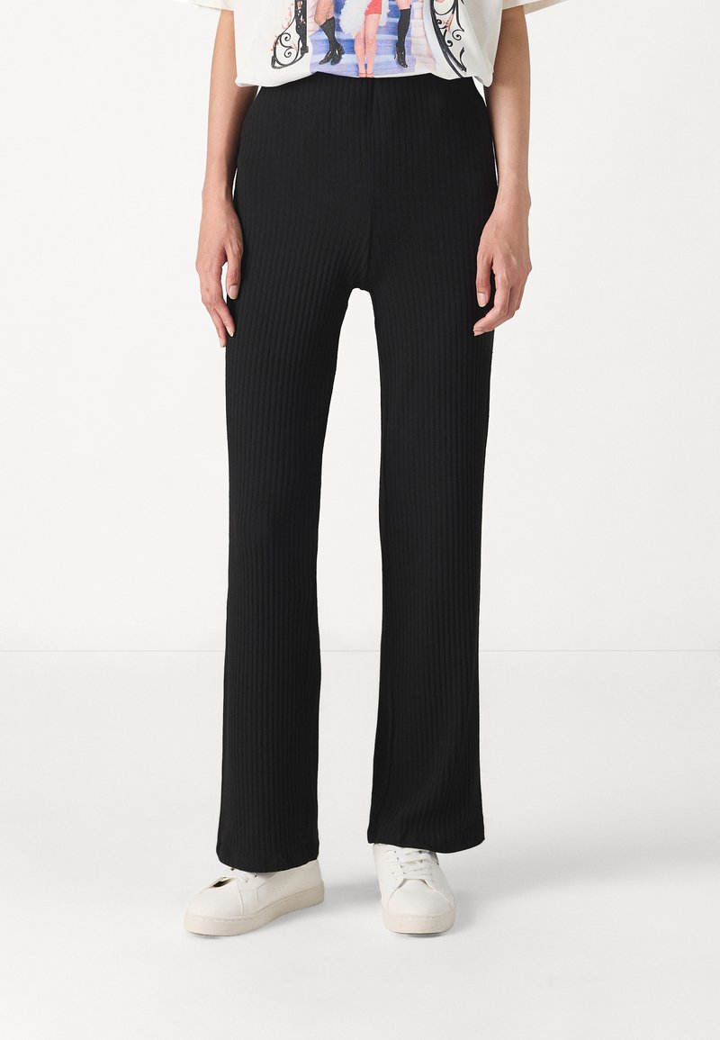 Pantalons noirs côtelés avec une coupe évasée, dotés d'une taille haute et d'un toucher doux. Associés à des baskets blanches.