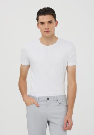 T-shirt bianco a righe con maniche corte e scollatura tonda, abbinato a pantaloni grigi chiari. Tessuto liscio con un design aderente.