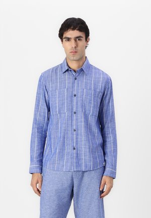 Chemise bleu à boutons avec des rayures verticales blanches, deux poches poitrine et des manches longues, fabriquée dans un tissu texturé. Associée à un pantalon assorti.