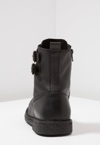 Bottes noires en cuir avec deux accents de boucle, finition texturée, languette de tirage et semelle en caoutchouc. La vue arrière met en évidence les détails de couture.