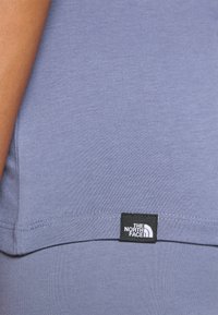 Svijetloplava pamučna majica s kratkim rukavima i crnom etiketom na donjem rubu s logotipom "The North Face". Glatka textura.