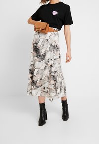 Czarna koszulka z motywem serca, długa spódnica w wężowy wzór w odcieniach beżu, czerni i brzoskwini, w połączeniu z czarnymi botkami na obcasie do kostki.