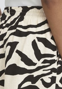 Jupe à taille élastique avec imprimé abstrait zébré noir et blanc, portée avec un haut côtelé gris clair et un segment de bras visible.