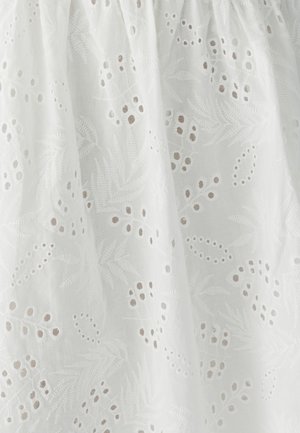 Tissu blanc brodé présentant des motifs complexes de feuilles et de fleurs, avec des découpes et des accents texturés dans des tons beige clair.