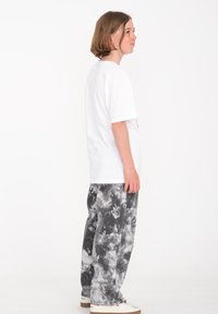 Camiseta blanca de algodón con mangas cortas, combinada con pantalones holgados de teñido anudado en negro y gris, y zapatillas beige.