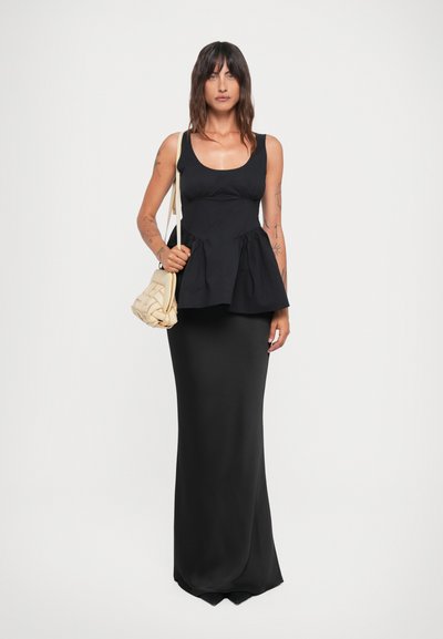 Schwarzes Peplum-Top mit taillierter Silhouette, kombiniert mit einem langen schwarzen Rock. Accessoires sind eine beigefarbene, geflochtene Umhängetasche.