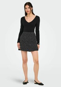 Sort langærmet bodysuit parret med en kort sort nederdel med et hvidt blomstermønster. Outfitet inkluderer sorte flade sko.