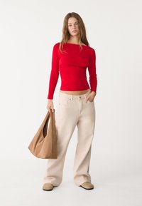 Rode lange mouwen top met een aansluitende snit, gecombineerd met brede beige broek. Een bruine suède schoudertas en beige klompen maken de look compleet.