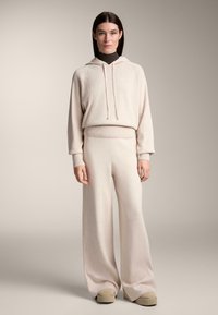 Svetlo béžová pletená mikina s rebrovým detailom, v kombinácii so širokými nohavicami z rovnakého materiálu. Mäkka textúra, tiahka pri kapucni a uvoľnený strih.