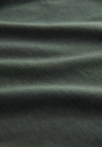 Tissu vert foncé avec une texture lisse, présentant des vagues et des plis subtils. Le matériau semble léger et doux.