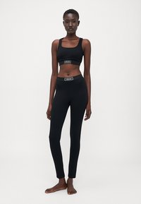 Set sportiv negru format dintr-un braletă cu un band logo și colanți cu talie înaltă, ambele realizate dintr-un material elastic pentru confort.