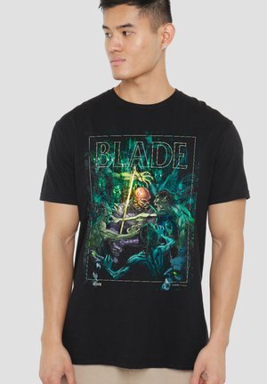 Junger Mann trägt ein schwarzes T-Shirt mit einer bunten Grafik eines Kriegers, der gegen Monster kämpft, und dem Wort "BLADE" auf der Vorderseite.