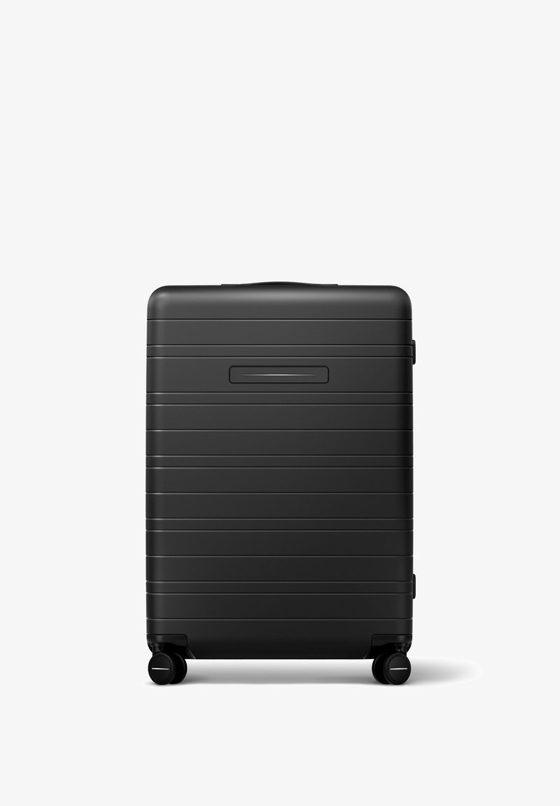 Valise rigide noire avec des rainures horizontales, poignée encastrée et quatre roues lisses pour une manœuvrabilité aisée.