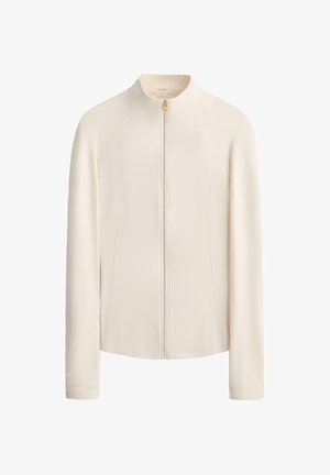 Krémově zbarvená bunda s dlouhým rukávem, předním zipem, kulatým límcem a jemnými šicími detaily podél stran a rukávů.