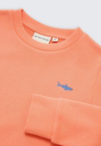 Korálová mikina s rebrovaným okrúhlym výstrihom a manžetami. Na prednej strane malá modrá výšivka žraloka. Mäkký materiál z bavlnenej zmesi.