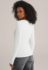 Witte lange mouwen top met een geribbelde textuur en een brede halslijn, gecombineerd met hoog-getailleerde grijze denim broeken met achterzakken.