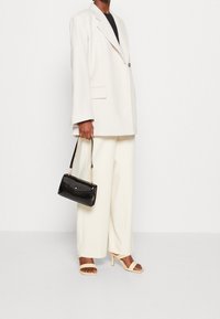 Bílý oversized blazer, černý top, krémové široké kalhoty, béžové sandály na podpatku a černá lakovaná kabelka se zlatým řetízkovým popruhem.