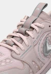 Κοντινός έλεγος ενός ροζ αθλητικού παπουτσιού Nike με αντίστοιχες κορδόνες, γκρι λεπτομέρειες και ασημένιο λογότυπο Nike swoosh σε πλέγμα και δερμάτινα πάνελ.