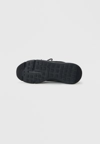 Calzado negro con suela de goma texturizada con patrones geométricos y una parte superior duradera. El diseño es funcional con un mínimo de detalles.