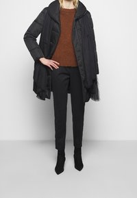 Piumino nero con ampio colletto, maglione marrone texturizzato, pantaloni neri su misura e stivaletti neri con punta a punta.