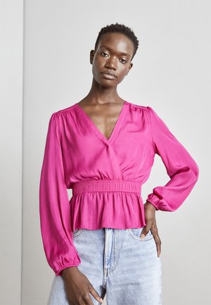 Fuchsia bluse med lange ærmer, en dyb V-hals og elastisk talje. Stilet med høj talje lys denim jeans. Glat tekstur.