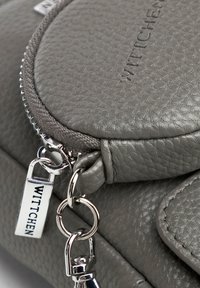 Borsa a tracolla in pelle grigia con superficie testurizzata, chiusura con zip e dettagli in metallo argentato, inclusi etichetta con logo e attacco per portachiavi.
