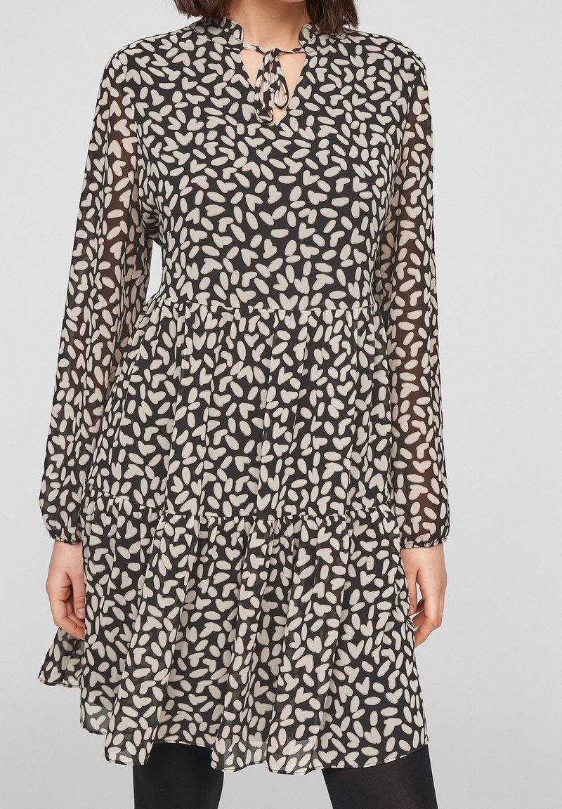 Femme portant une robe à manches longues à motif noir et blanc avec un col trou de serrure noué et une jupe ample à étages.