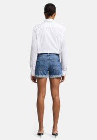 Shorts en denim, bleus, avec un ourlet effiloché. Associés à une chemise blanche à col, à manches longues. Texture lisse, design ajusté.