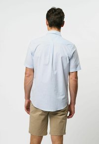 Lichtblauw shirt met korte mouwen, met een rugplooi en een button-down kraag, gecombineerd met beige shorts. Zachte stof met een gladde textuur.