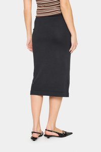 Fustă creion neagră, până la genunchi, cu textură netedă și finisaj tivuit, asortată cu pantofi negri cu barete și accente cu ținte.