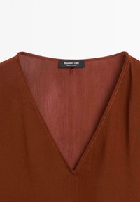 Vêtement de couleur rouille à col en V avec des coutures visibles et une étiquette Massimo Dutti cousue à l'intérieur du col.