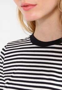 Czarna i biała koszulka w paski z okrągłym dekoltem i krótkimi rękawami. Tkanina wydaje się miękka o gładkiej fakturze. Prosty design.