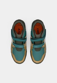 Turquoise and tan athletic shoes with a textured surface, dual Velcro straps, and white accents, featuring a padded collar and orange insoles.