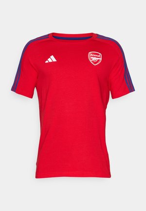 T-shirt rouge à manches courtes en tissu coton, avec un col rond, des rayures bleues aux épaules et un logo d'Arsenal sur la poitrine.