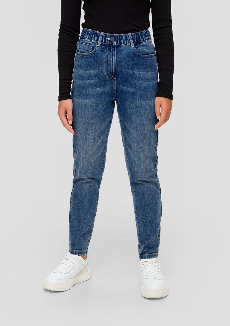 Svijetloplavi traperice s visokim strukom, s prednjim džepovima, s patentnim zatvaračem i suženim nogavicama, uparene s bijelim tenisicama.