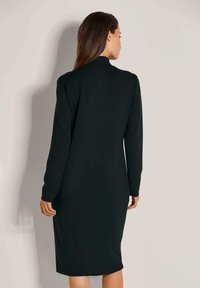 Schwarzes langärmliges Kleid mit hohem Kragen, figurbetontem Design, knielang, glatte Textur, minimalistischer Stil, keine sichtbaren Muster oder Akzente.