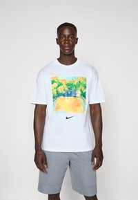 Hvid kortærmet t-shirt med et farverigt akvarel-grafik af en basketballbane, med et sort Nike-logo nederst.