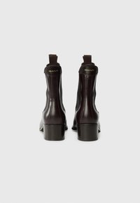 Bottes chelsea en cuir marron avec un bout carré, panneaux latéraux élastiques et un petit talon carré. Détail de logo doré à l'arrière. Texture lisse.