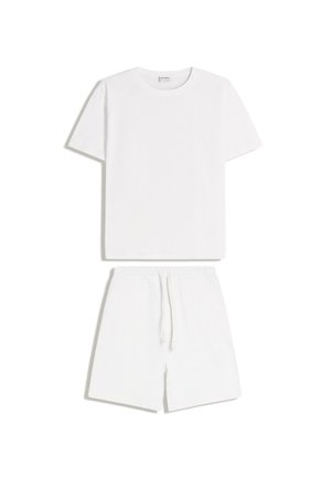 Fehér rövid ujjú, kerek nyakú póló, fehér, elasztikus derékpántos rövidnadrággal párosítva, amelyen zsinóros megkötő és oldalzsebek találhatók.