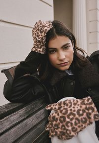 Handschoenen met luipaardprint van zachte stof met een ontspannen pasvorm. Het ontwerp bevat donkerbruine bontaccenten, gecombineerd met een bruine jas en trui.