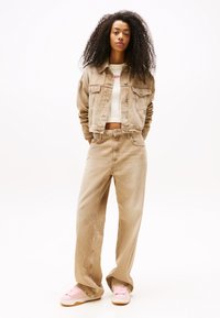 Beige denimjakke og matchende vidde bukser, kombinert med en hvit kortermet genser og rosa sneakers. Modellen står med hendene i lommene.