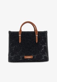 Bolso negro con superposición de encaje floral, asas de cuero marrón con costuras blancas y una pequeña placa de logo marrón en la parte delantera.