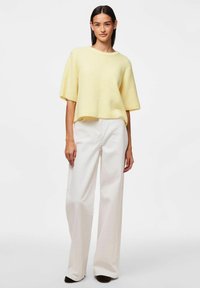 Żółty prążkowany top z krótkim rękawem w połączeniu z białymi spodniami o szerokiej nogawce. Stylizacja charakteryzuje się luźnym krojem i miękką fakturą.