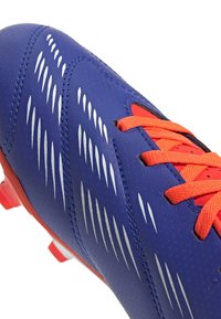 Bota de fútbol azul con una superficie lisa y texturizada, que cuenta con cordones naranjas, rayas de acento plateadas y un interior rojo.