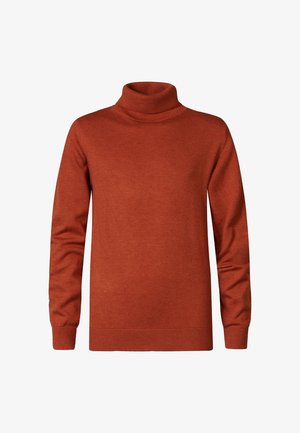 Rust-orange turtleneck sweater, gray slim-fit jeans, white sneakers with maroon accents, standing on a plain background.