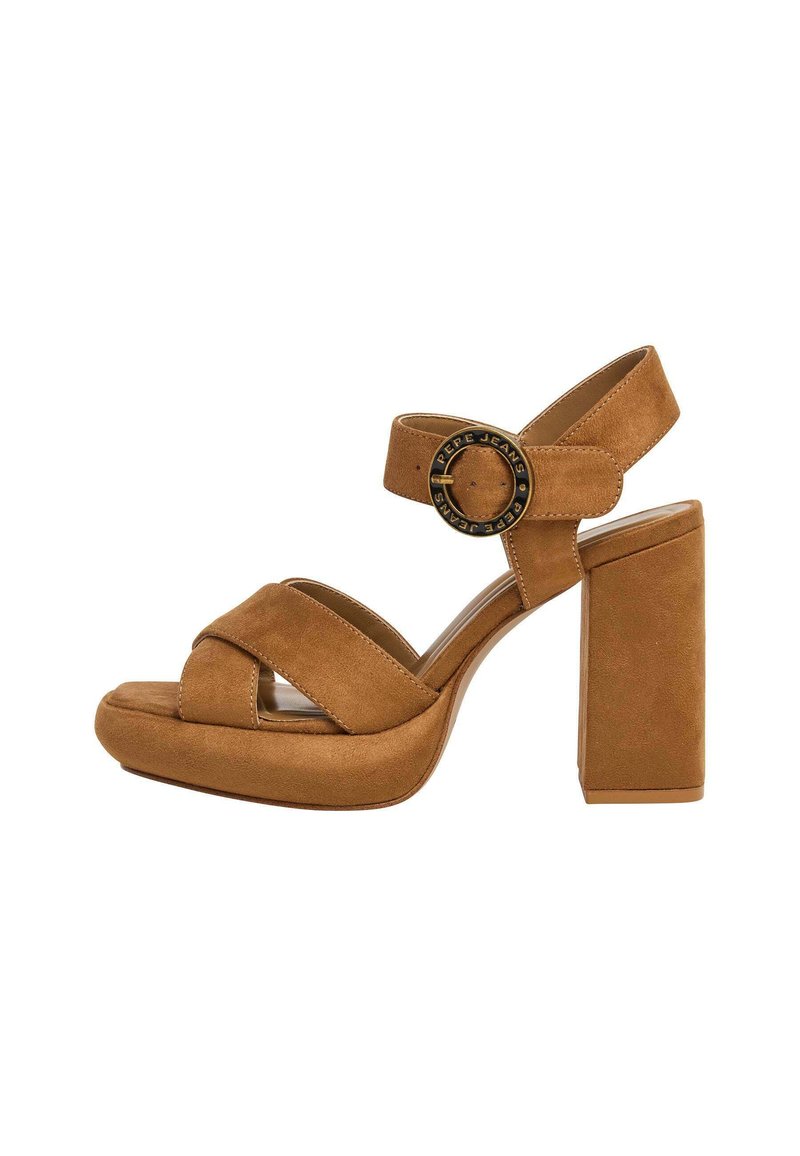Sandali con tacco in suede marrone, dotati di suola a piattaforma, ampi lacci incrociati e dettaglio di fibbia metallica circolare sulla cinghia alla caviglia.