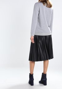 Gray sweatshirt with long sleeves and a ribbed hem, paired with a black pleated skirt and navy high-heeled ankle boots.