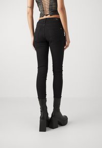 Jeans skinny neri con vita alta, caratterizzati da un leggero lavaggio e tasche posteriori, abbinati a stivali neri con tacco chunky.