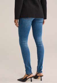 Tajta jeans i en medelblå tvätt, med en slät textur, subtila blekningar och en standard midja. I kombination med svarta klackskor.