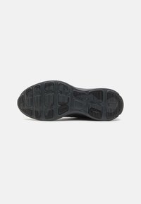 Semelle en caoutchouc noir d'une chaussure de sport avec motif sur la semelle et petit logo Nike Swoosh près du talon sur fond uni.